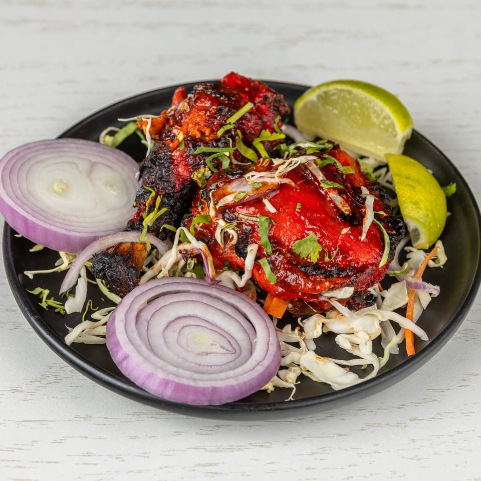 Spice Mantra's vibrant red Indian chicken tikka, garnished with fresh cilantro, onions, and lime wedges.