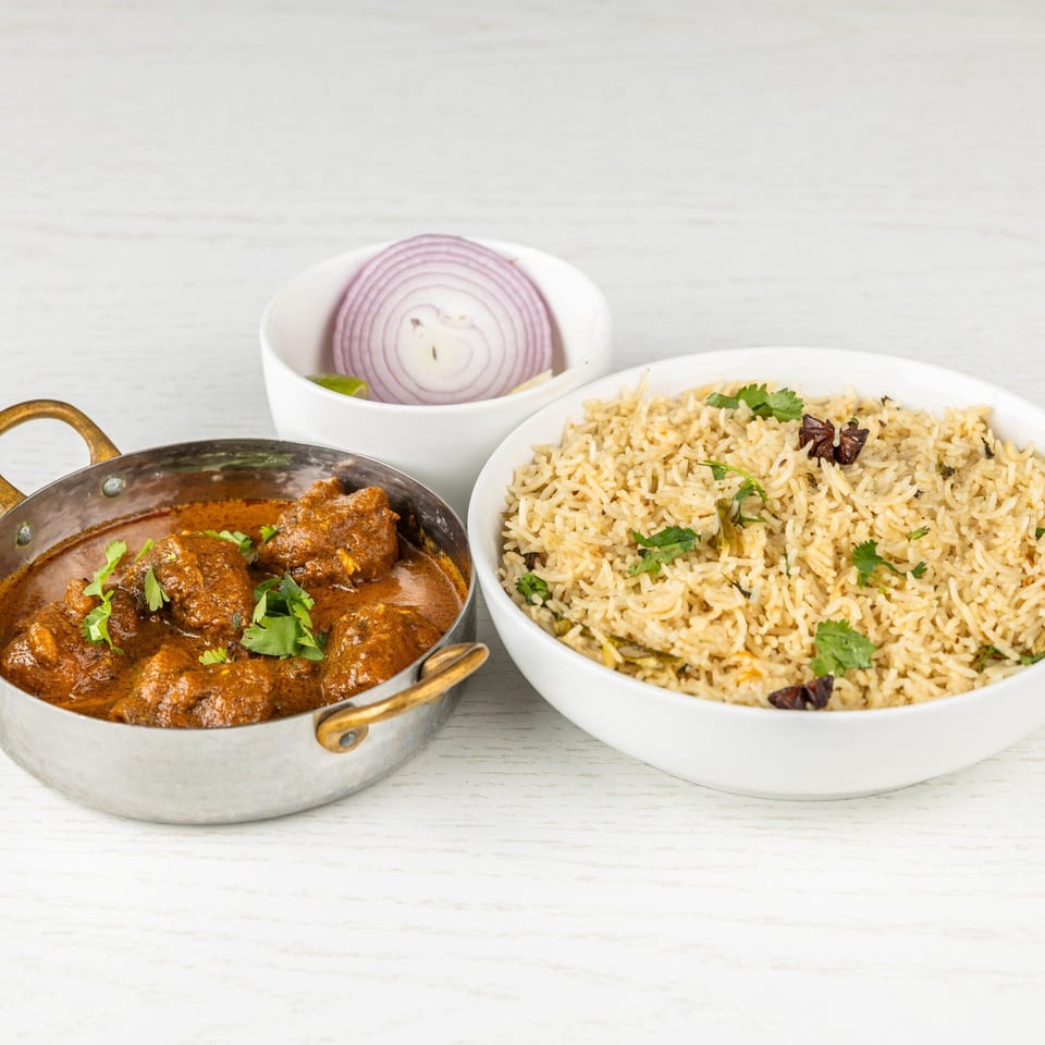 Spice Mantra's Indian chicken curry in a brass pot with rice and sliced red onions.