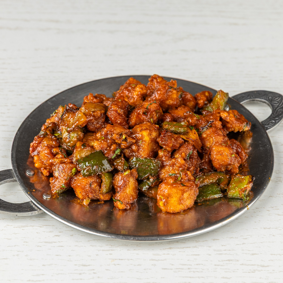 Spice Mantra's chili paneer, a vibrant Indian dish with red-orange paneer and green peppers on a metal plate.
