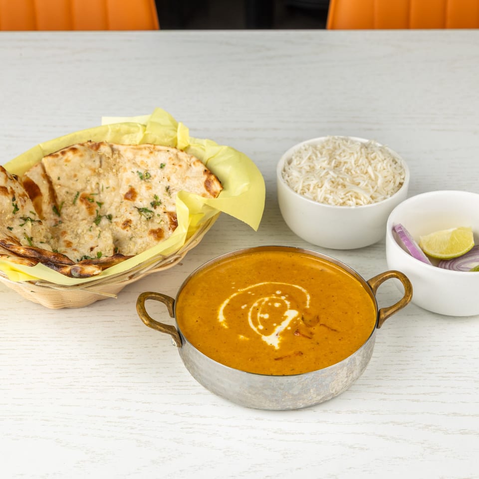 Indian meal with naan bread, rice, dal makhani, and a side of sliced red onion and lime.