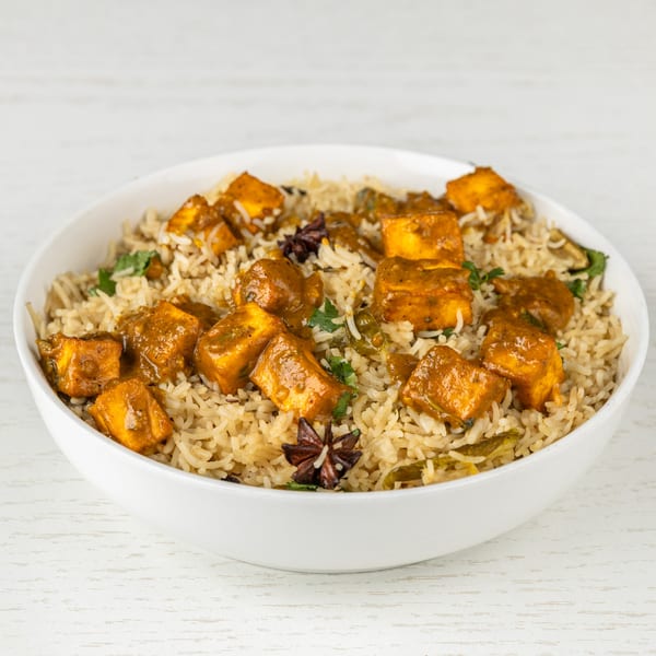 Indian paneer biryani with rice, paneer cubes, and star anise in a white bowl.