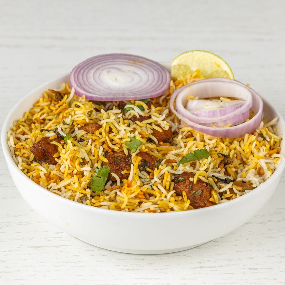 Chicken Biryani from Spice Mantra, garnished with red onion rings, cilantro, and a lemon wedge.