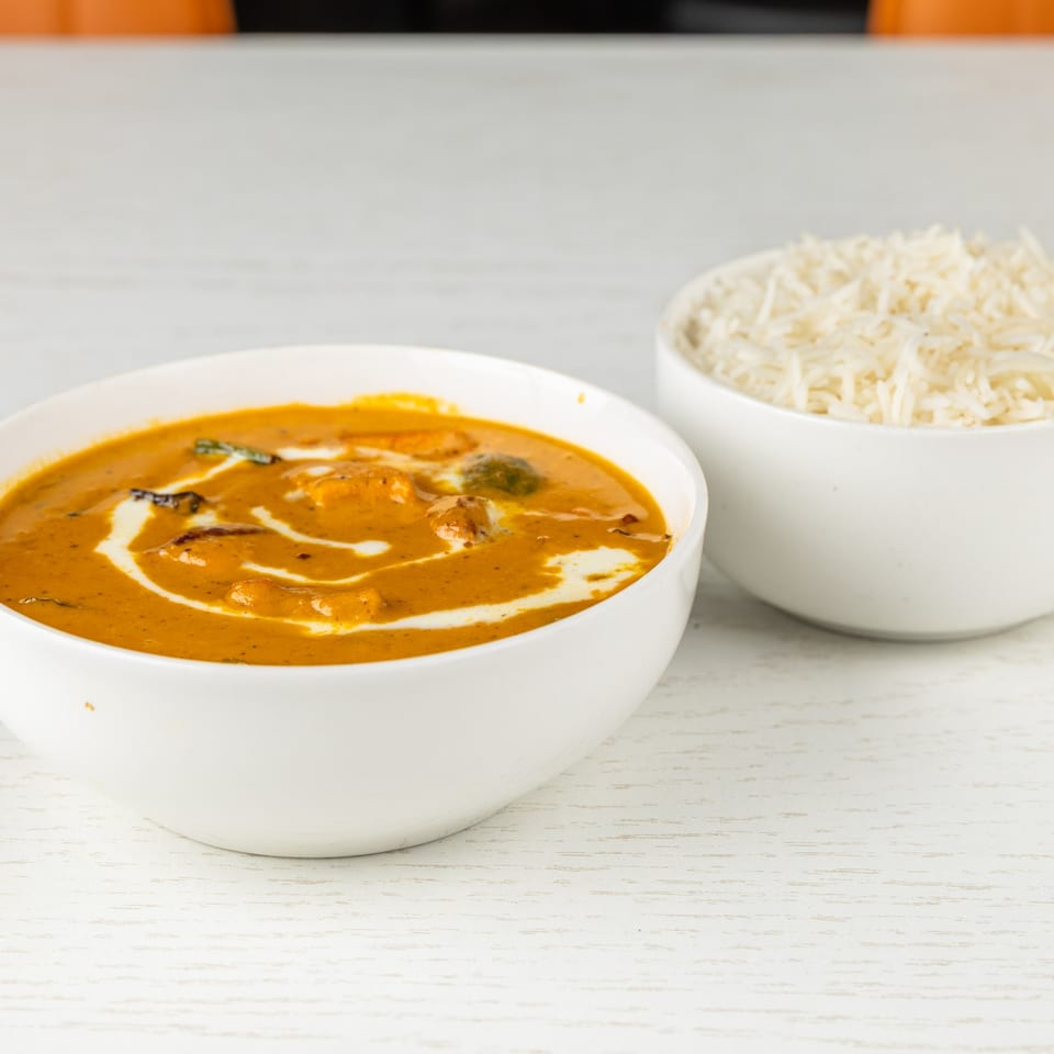 A bowl of creamy Indian curry with swirls of white sauce, alongside a bowl of white rice.