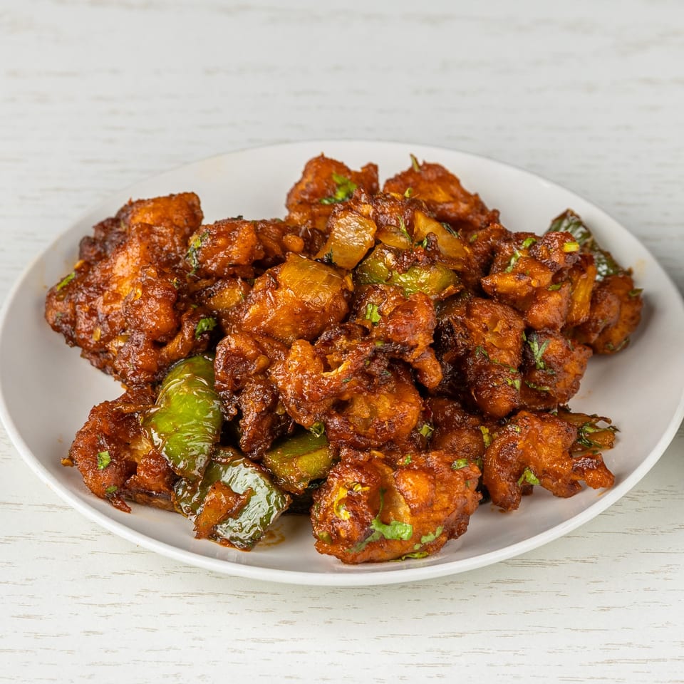 A white plate filled with Gobi Manchurian, featuring crispy cauliflower florets in a spicy, dark sauce.