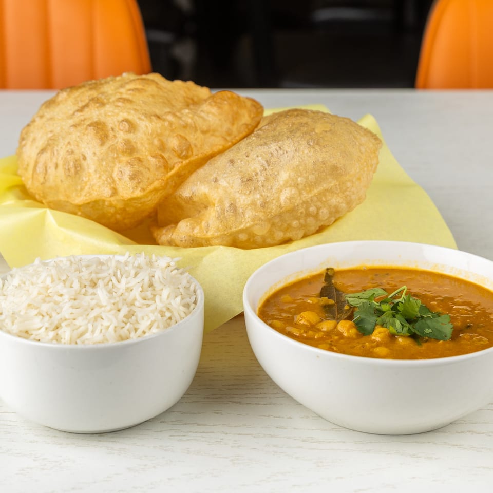 Two golden-brown fried puri breads, a bowl of white rice, and a bowl of chana masala.
